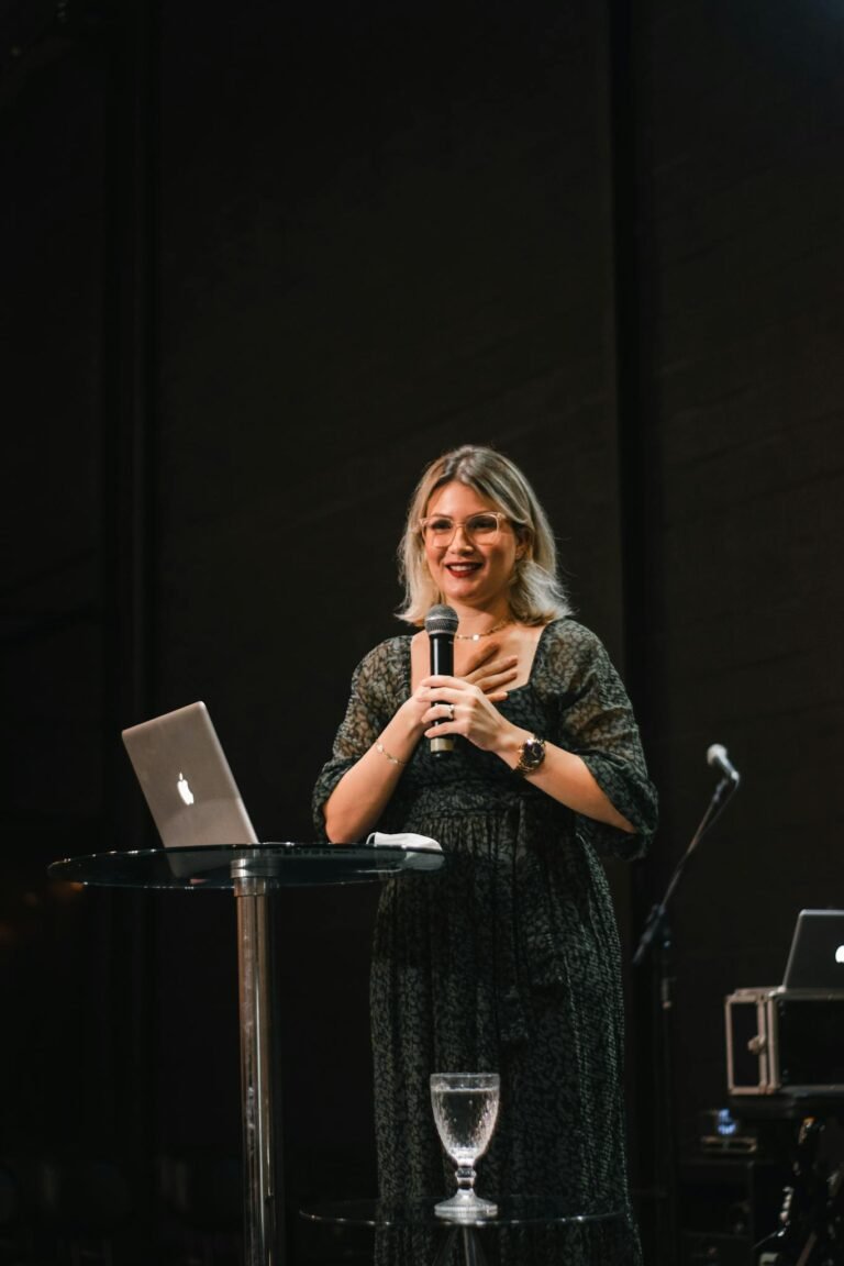A woman giving a presentation on stage with a microphone and laptop.